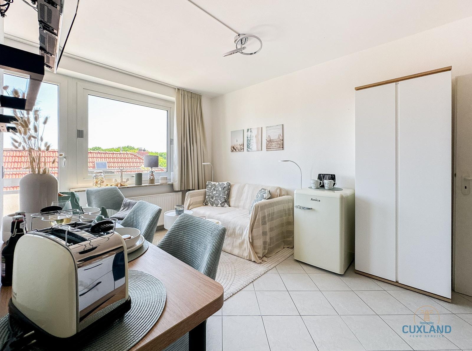 Wohn- und Essbereich mit Sofa, Küchenzeile und Fensterblick auf Dächer.