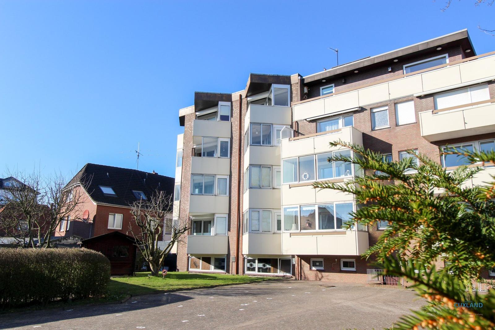Modernes Mehrfamilienhaus mit Balkonen und Glasfronten. Grünfläche und Bäume im Vorgarten.