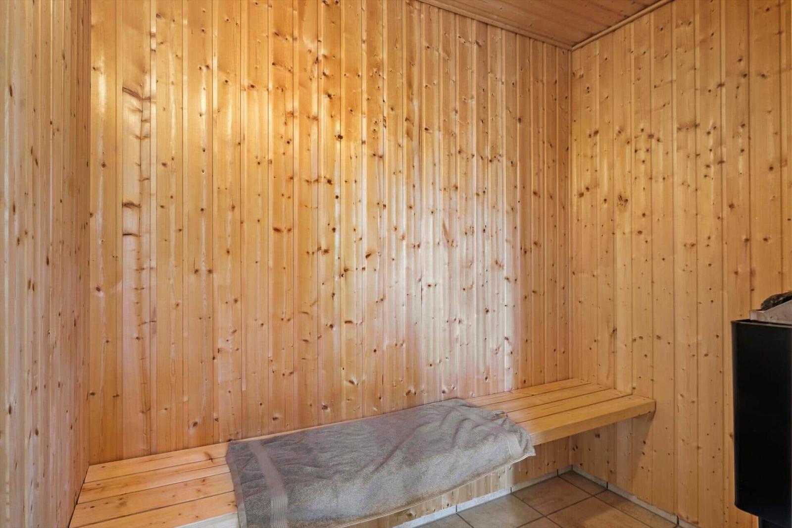 Sauna with wooden walls and bench, on which lies a gray towel.