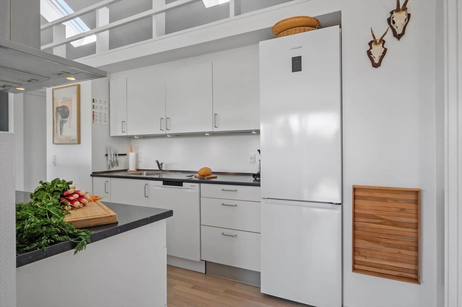 Kitchen with white cabinets, black countertop, and refrigerator. Wooden floor and wall decor.