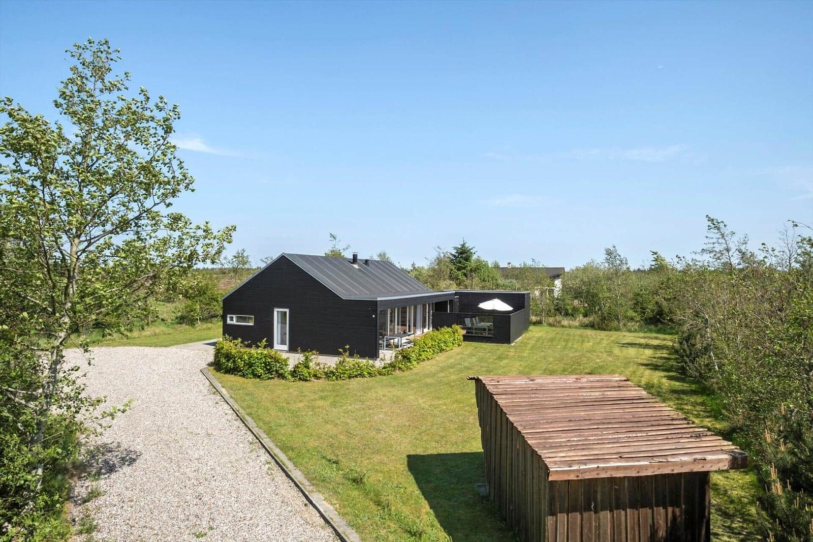 Black house with terrace and garden. Wooden shed in foreground.
