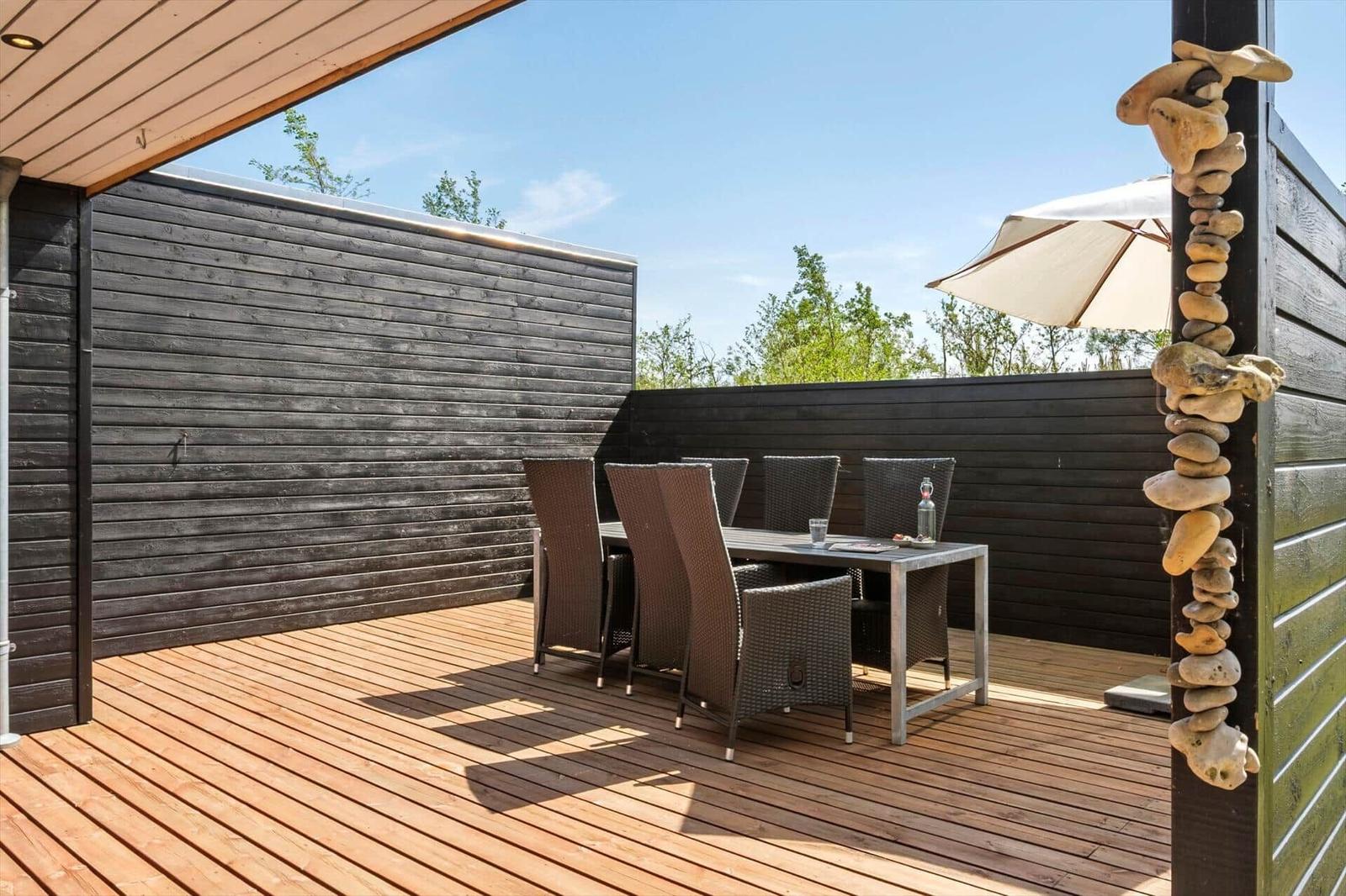 Terrace with table, chairs, and umbrella. Wooden deck and dark wooden wall.