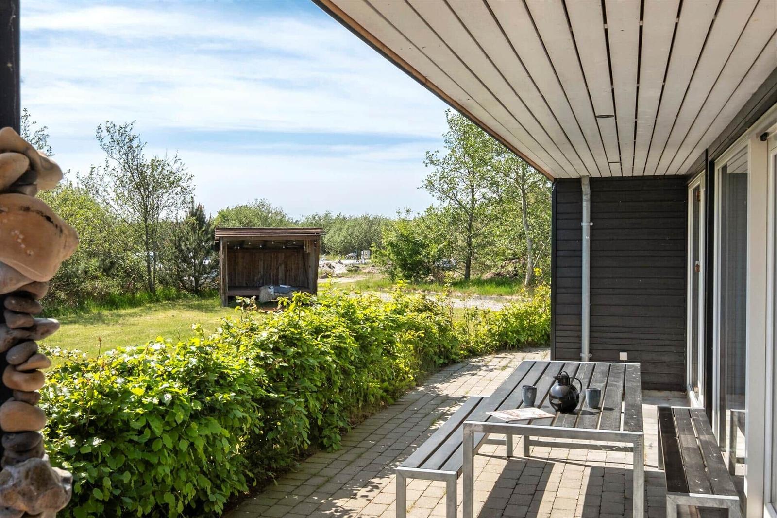 Patio with table and benches, view of garden and wooden shed.