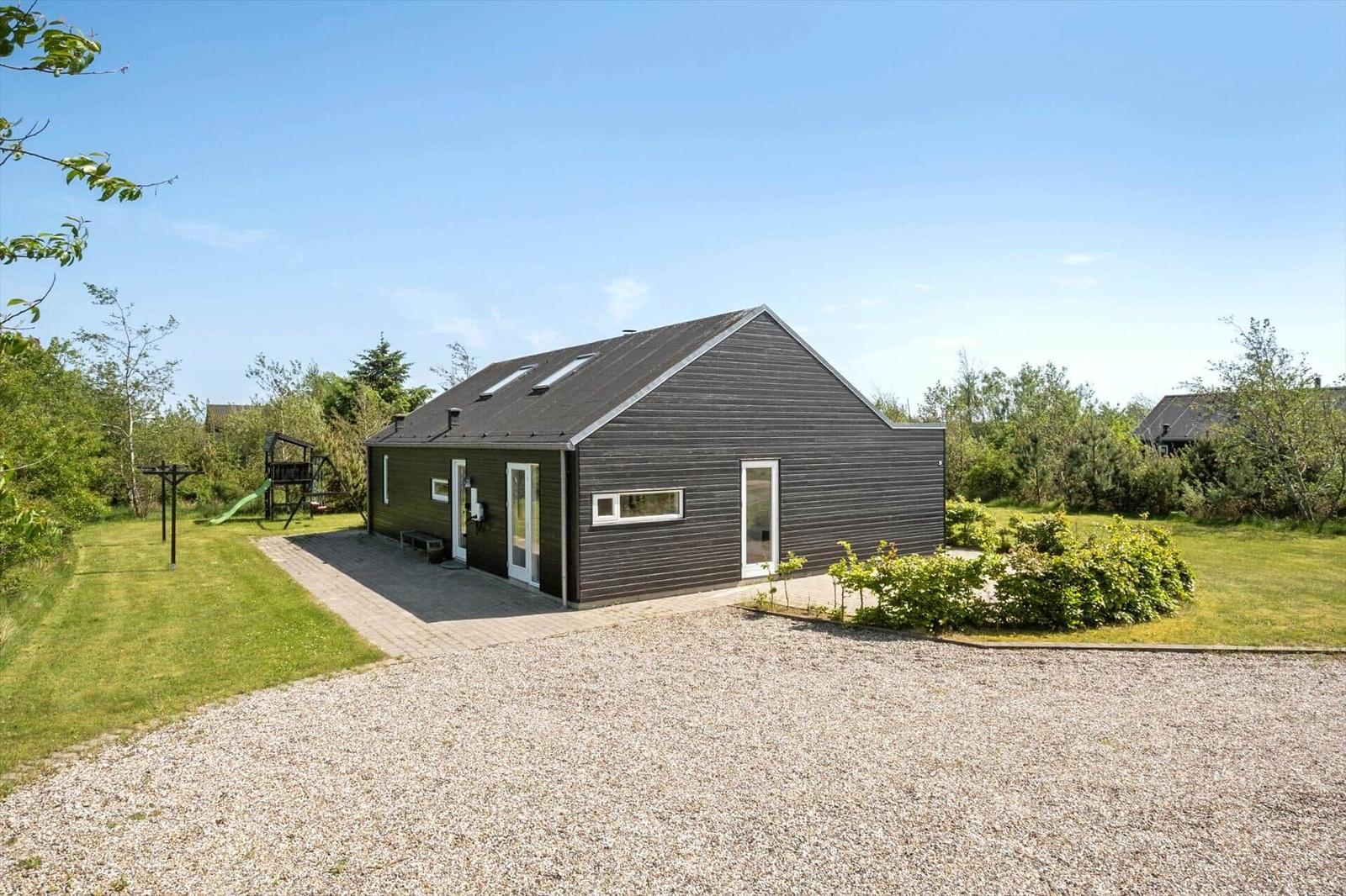 Modern wooden cabin with garden and playground under blue sky.