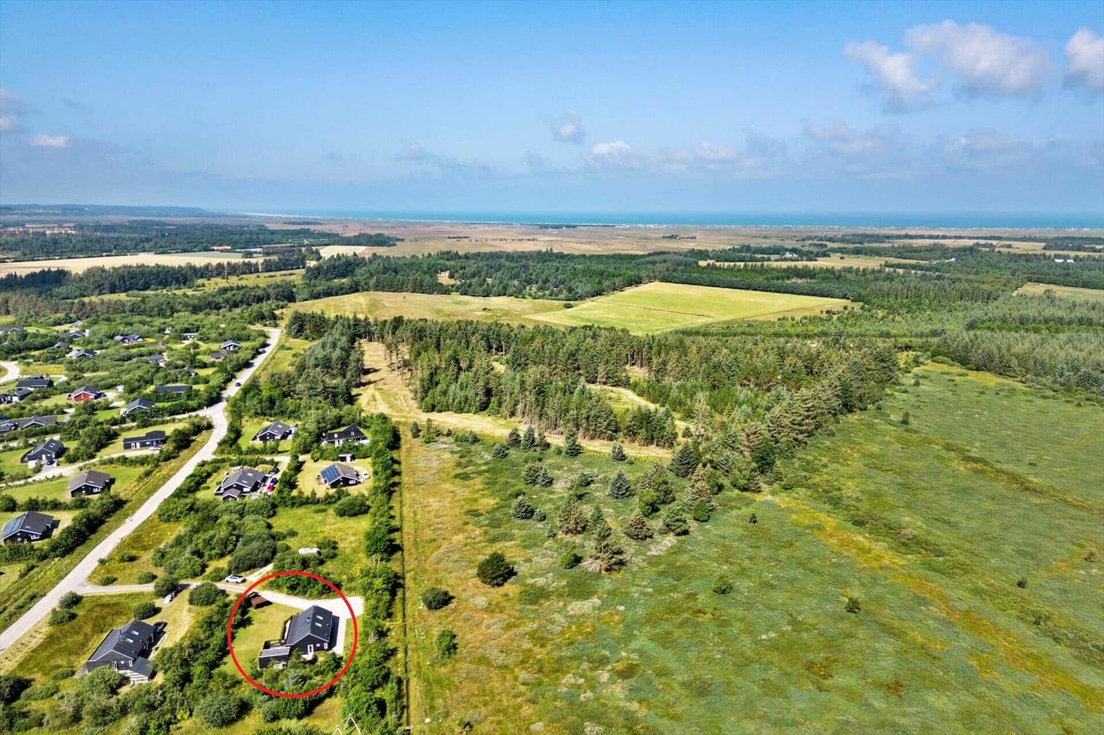 A house in a green landscape with forest and fields, ocean in the background.