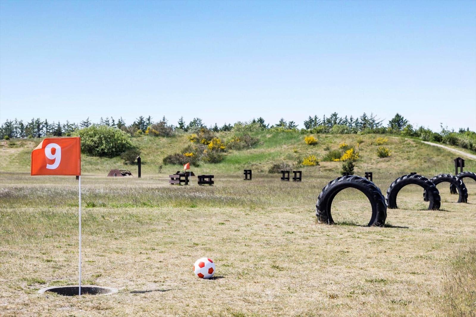 Golf course with hole 9, ball, and tire obstacles on green ground.