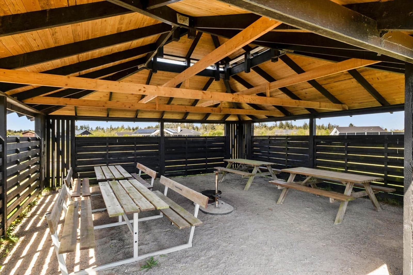 Shaded wooden outdoor area with multiple picnic tables and grill spot.