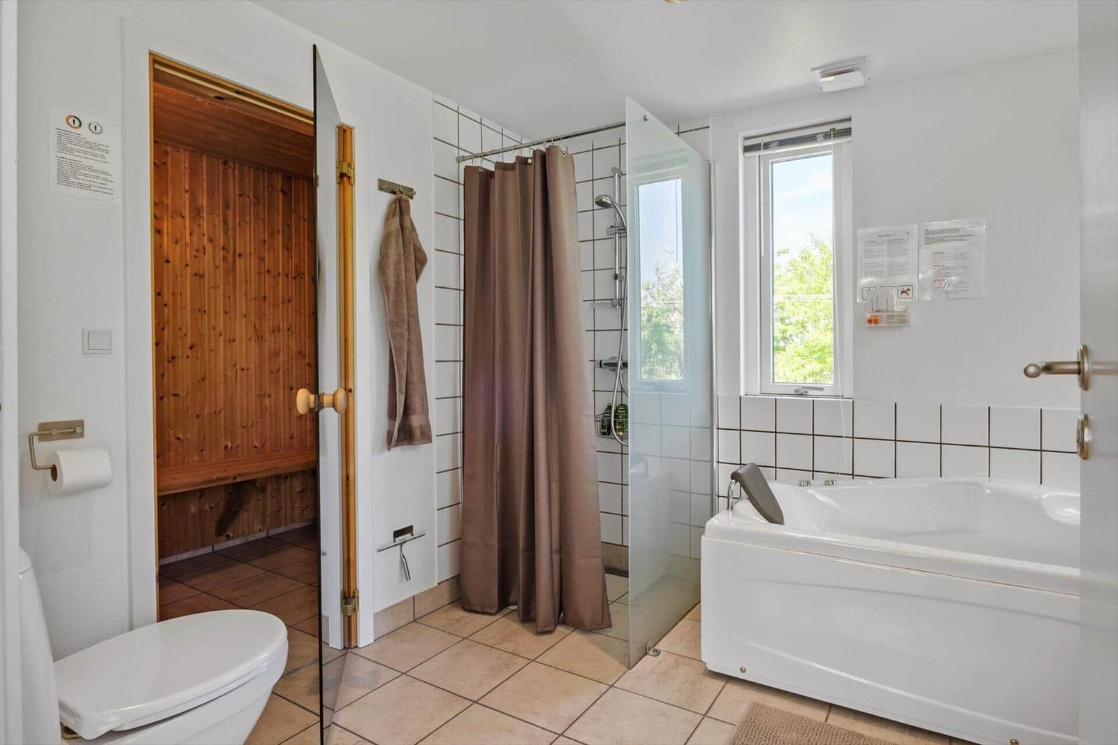 Bathroom with shower, bathtub, and sauna. Window with view of greenery.