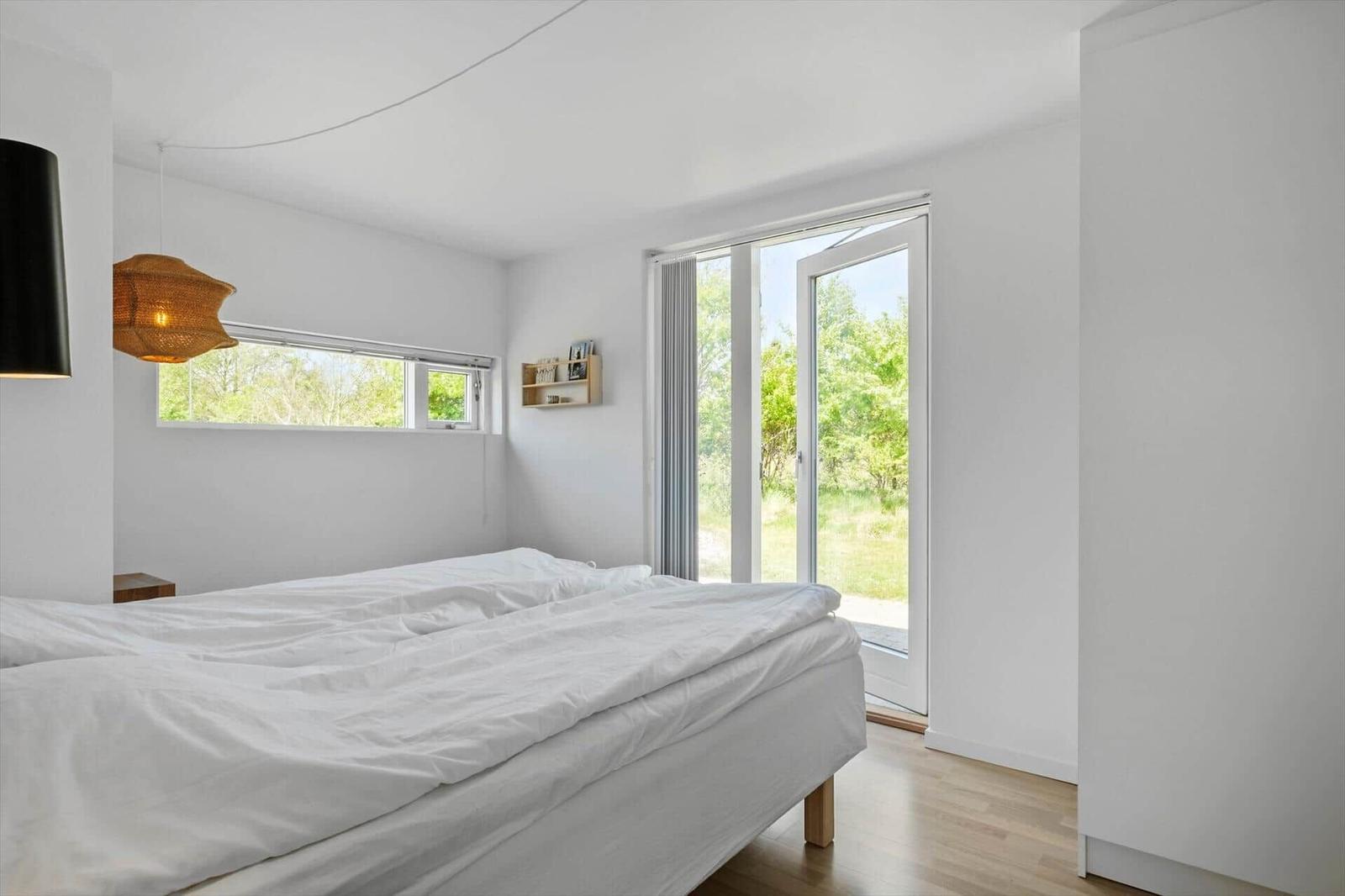 Bedroom with double bed, large windows, and view of greenery.