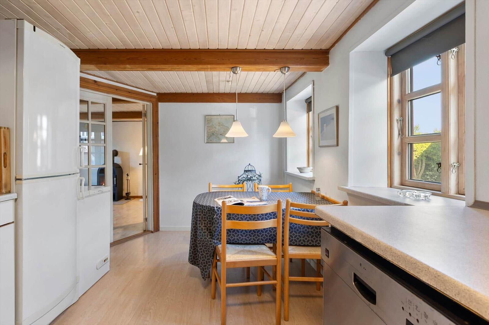 Kitchen with dining area, wooden ceiling, and window. Refrigerator, sink, and dining table with chairs.