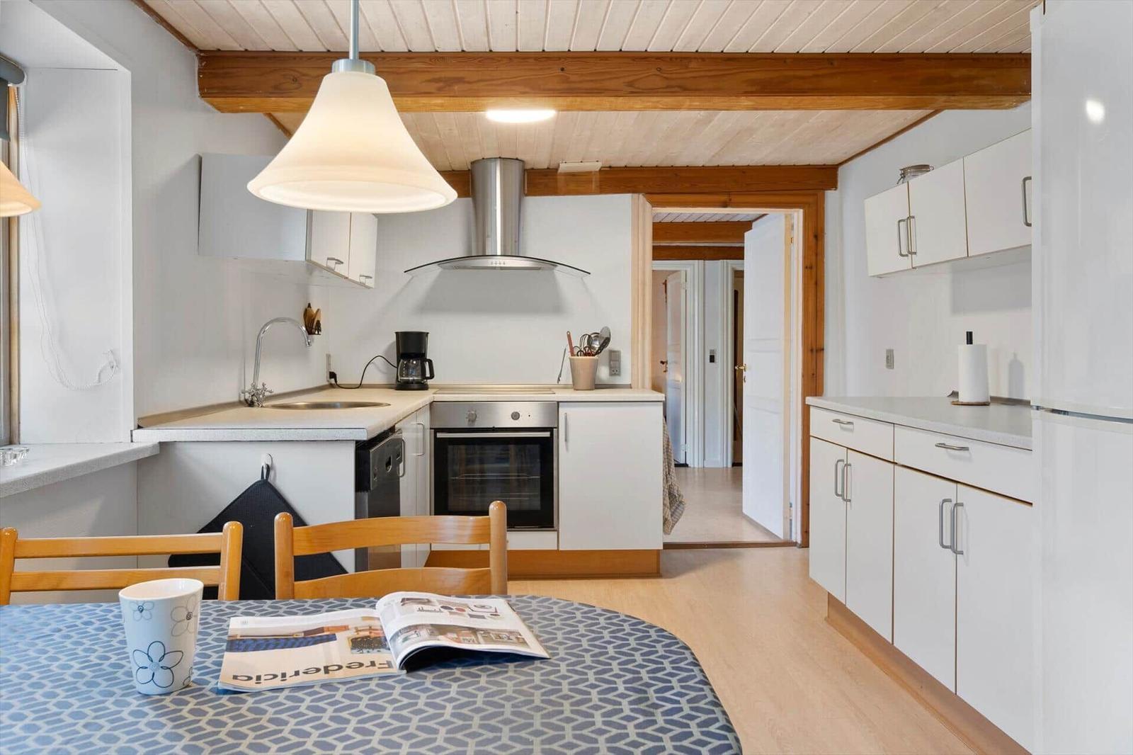 Kitchen with dining area, white cabinets, and wooden beams on ceiling.