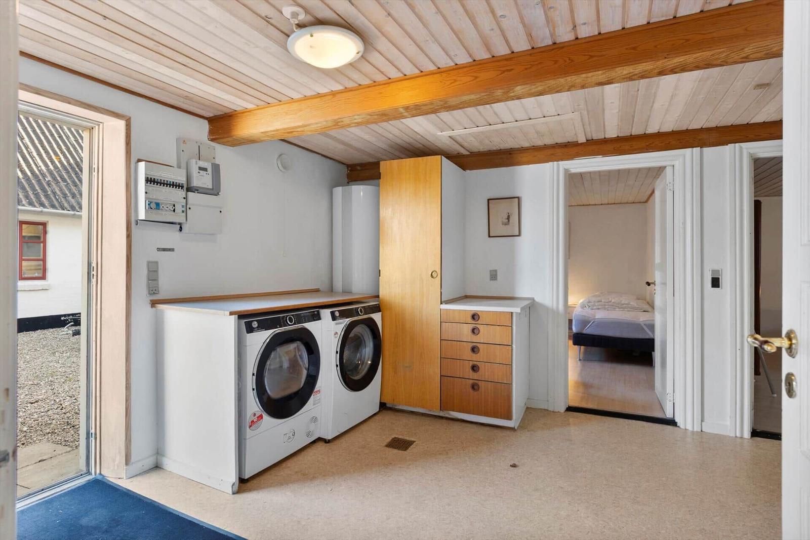 Laundry room with washer and dryer, wooden beam ceiling, view into bedroom.