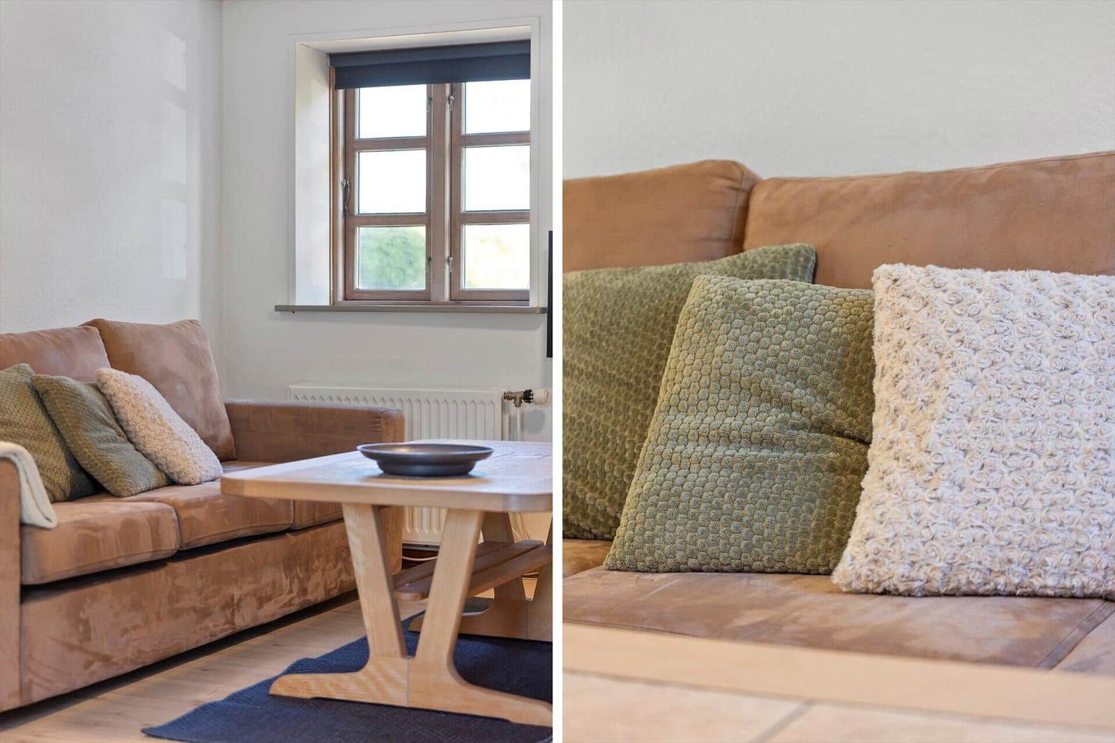 Living room with brown sofa, green and white cushions, wooden table, and window.