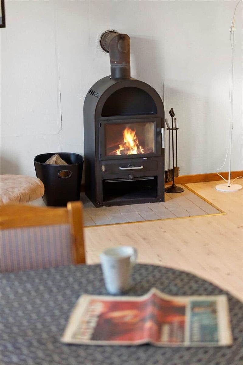 A wood-burning stove stands in a room with wooden floor and table in the foreground.