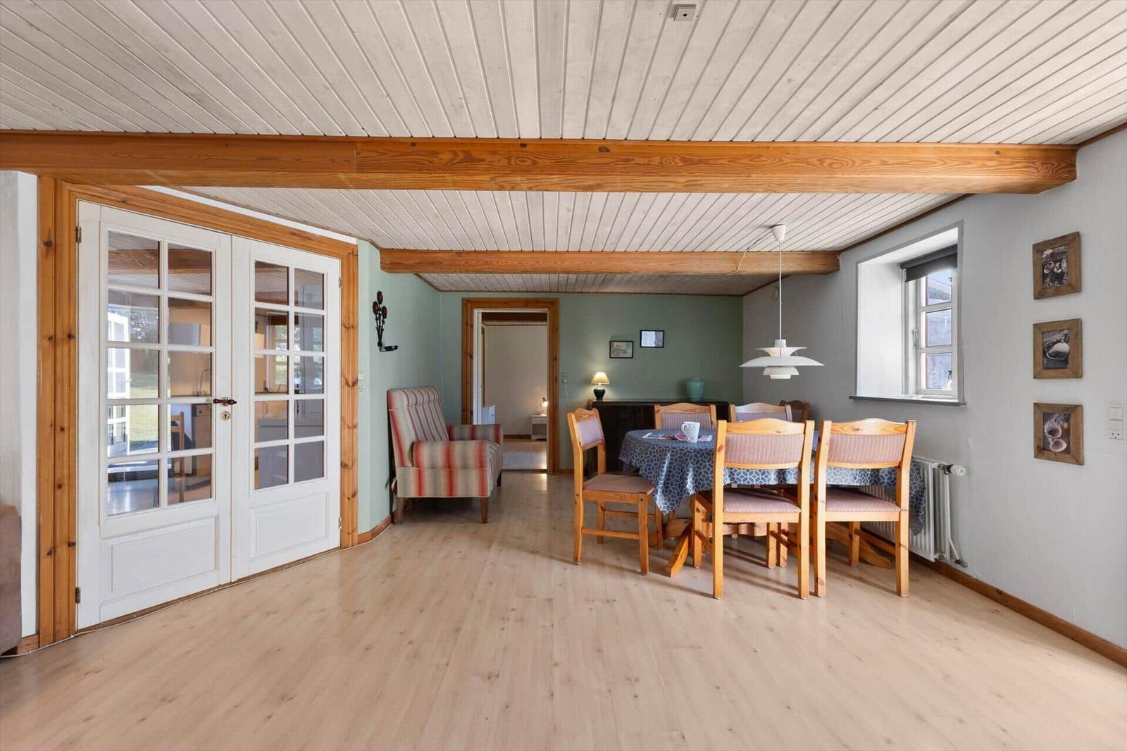 Dining room with wooden table, chairs, and window. Stairs and door in the background.