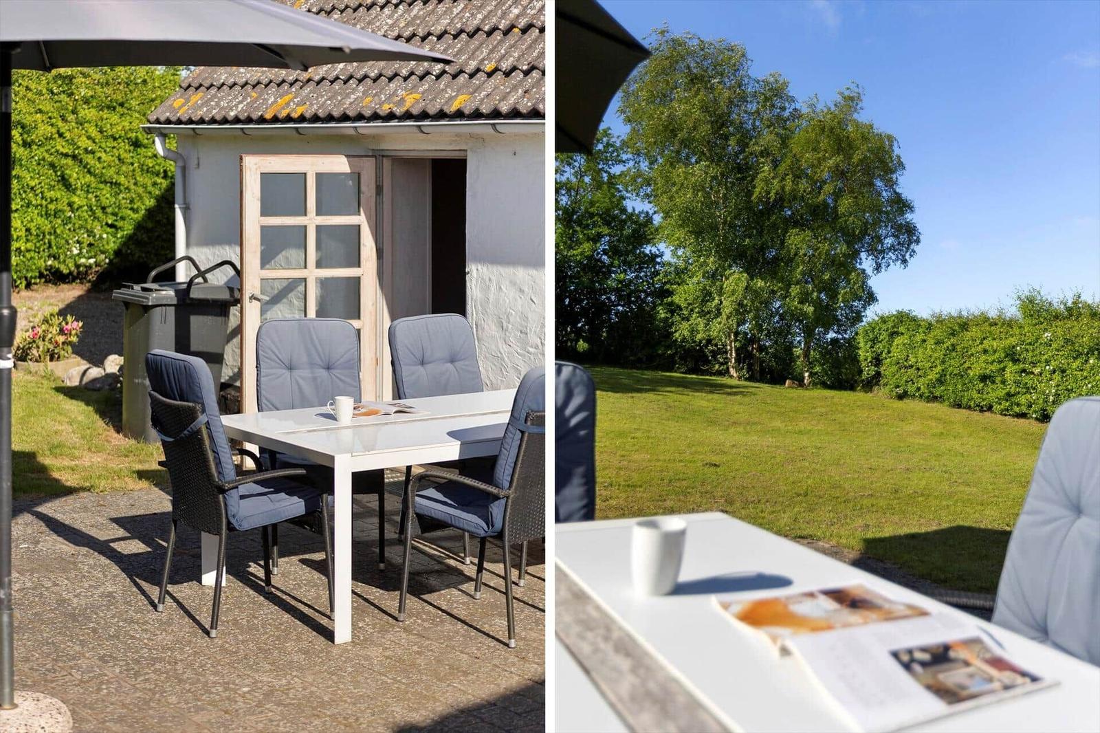 Outdoor area with table, chairs, and umbrella in front of a house with garden.