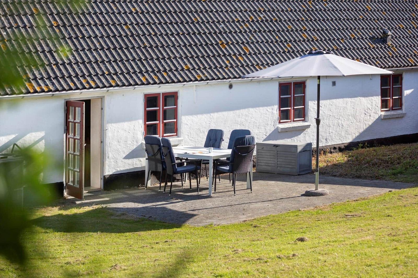House with terrace, table, chairs, and umbrella. White exterior wall and red windows.