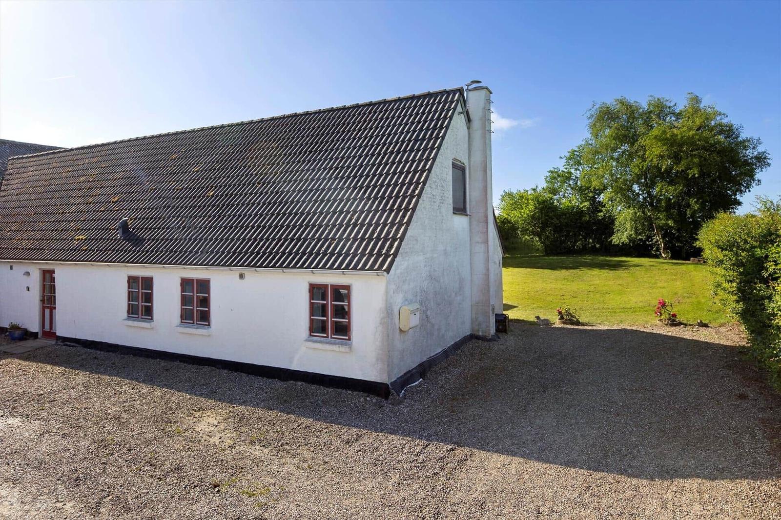 A white house with red window frames and a black roof on a gravel area.
