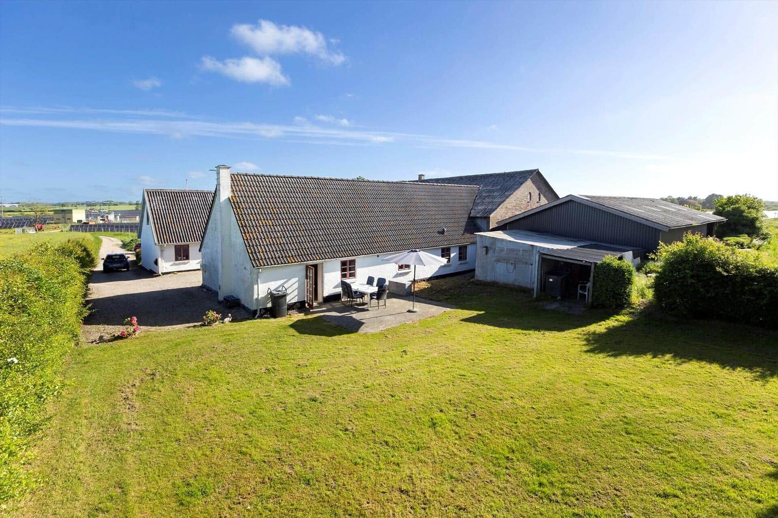 House with garden, terrace, and umbrella. Outbuildings and green surroundings.