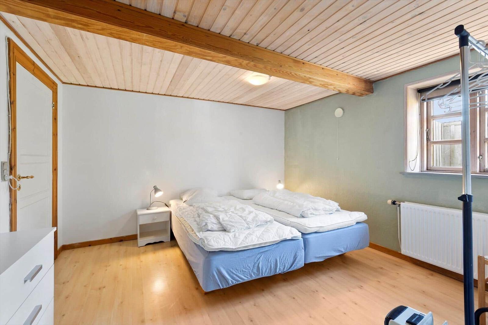 Room with double bed, wooden ceiling, and window. A nightstand is next to the bed.