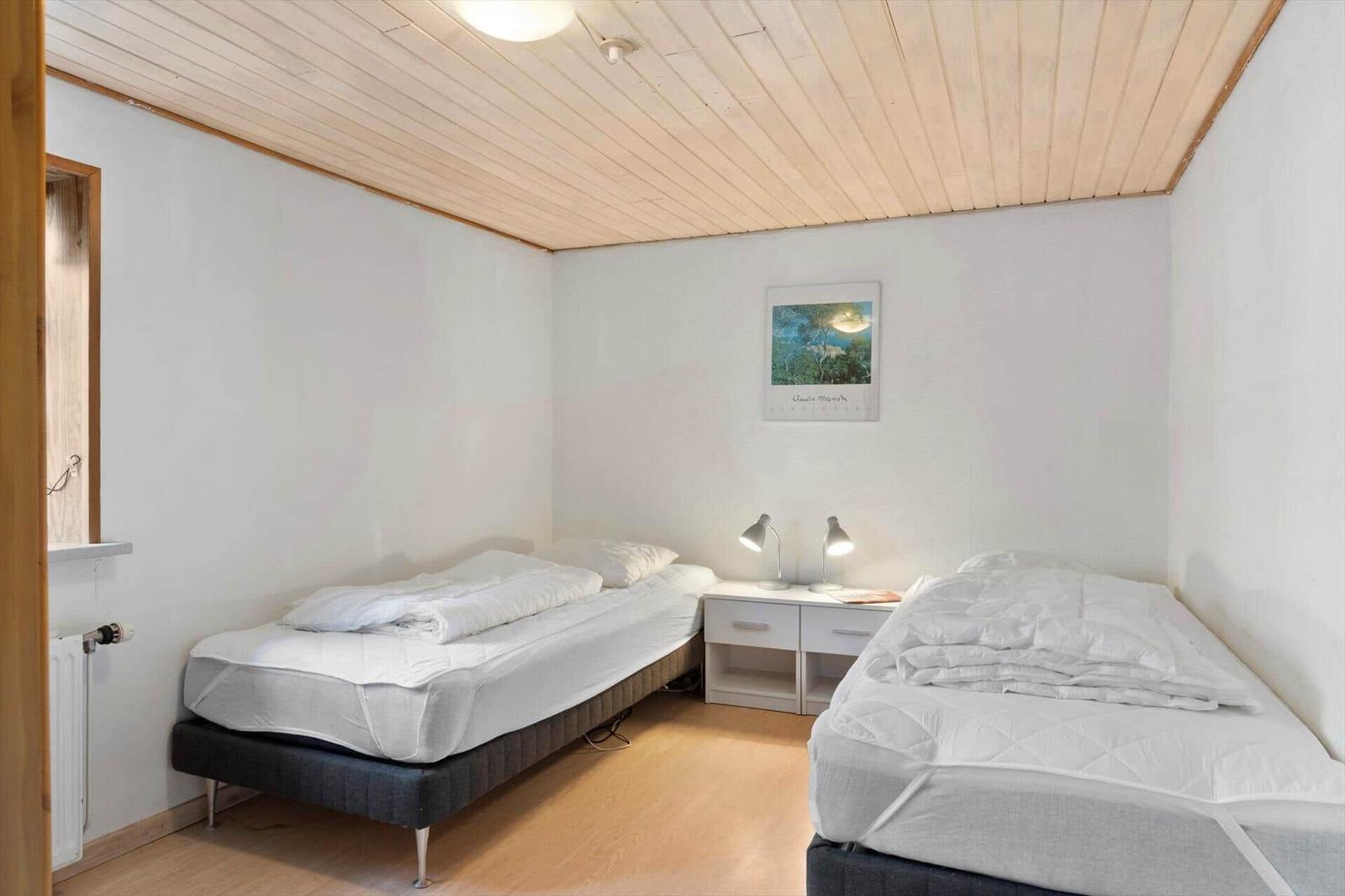 Two beds with white bedding, nightstand with lamps and picture on the wall.