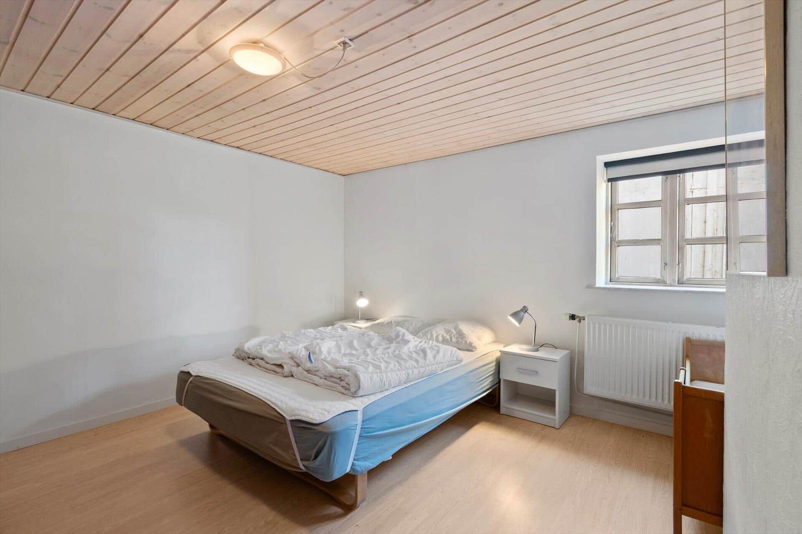 Bedroom with bed, nightstand, and window. Wooden ceiling and floor.