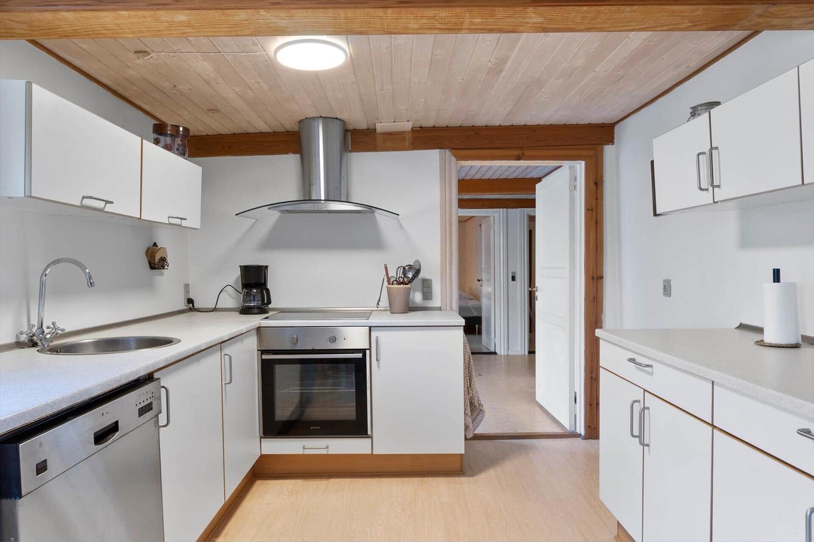 Kitchen with white cabinets, stainless steel sink, and oven under wooden ceiling.