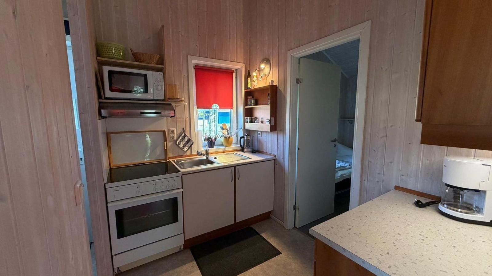 Küche mit Herd, Spüle und Fenster. Tür führt in Schlafzimmer.