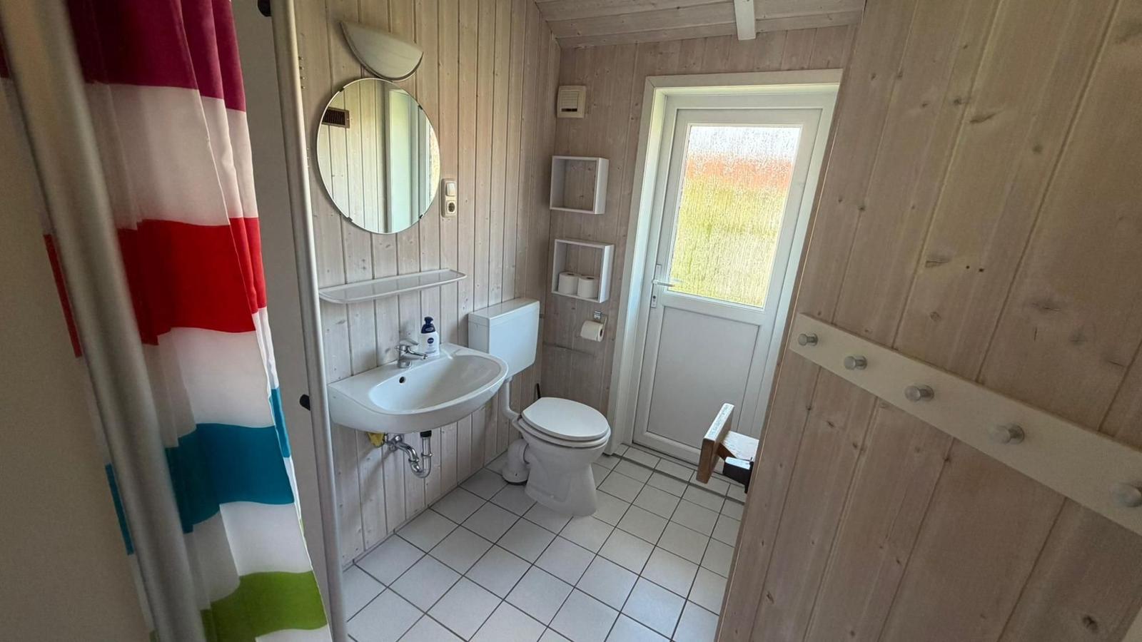 Bad mit Dusche, Waschbecken und Toilette. Holzwände und Fliesenboden.