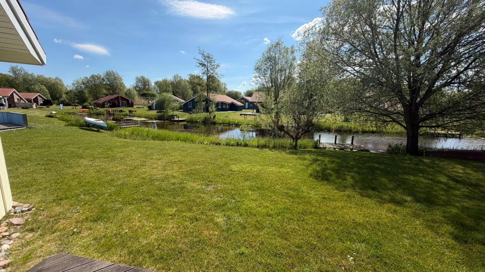 Grüner Rasenbereich mit See und mehreren Häusern im Hintergrund.