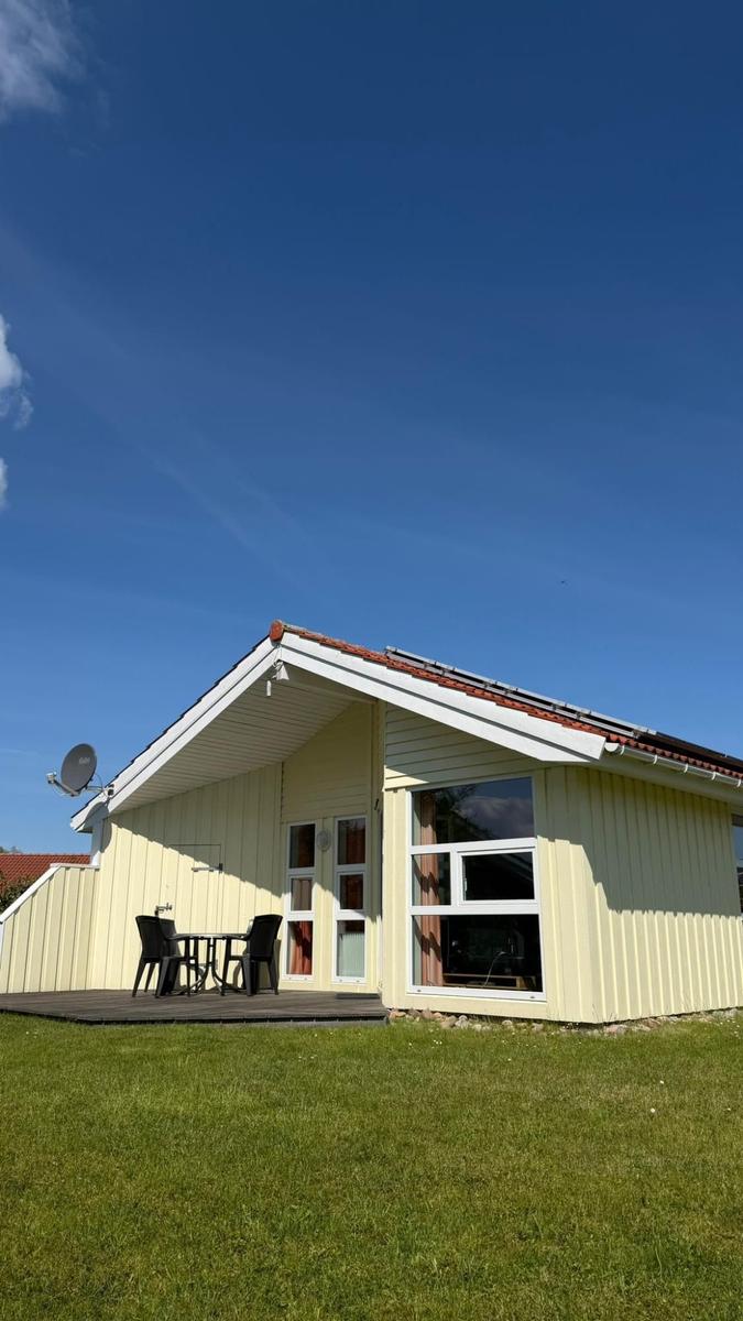 Ein gelbes Ferienhaus mit Terrasse, Tisch und Stühlen. Hintergrund: klarer Himmel.