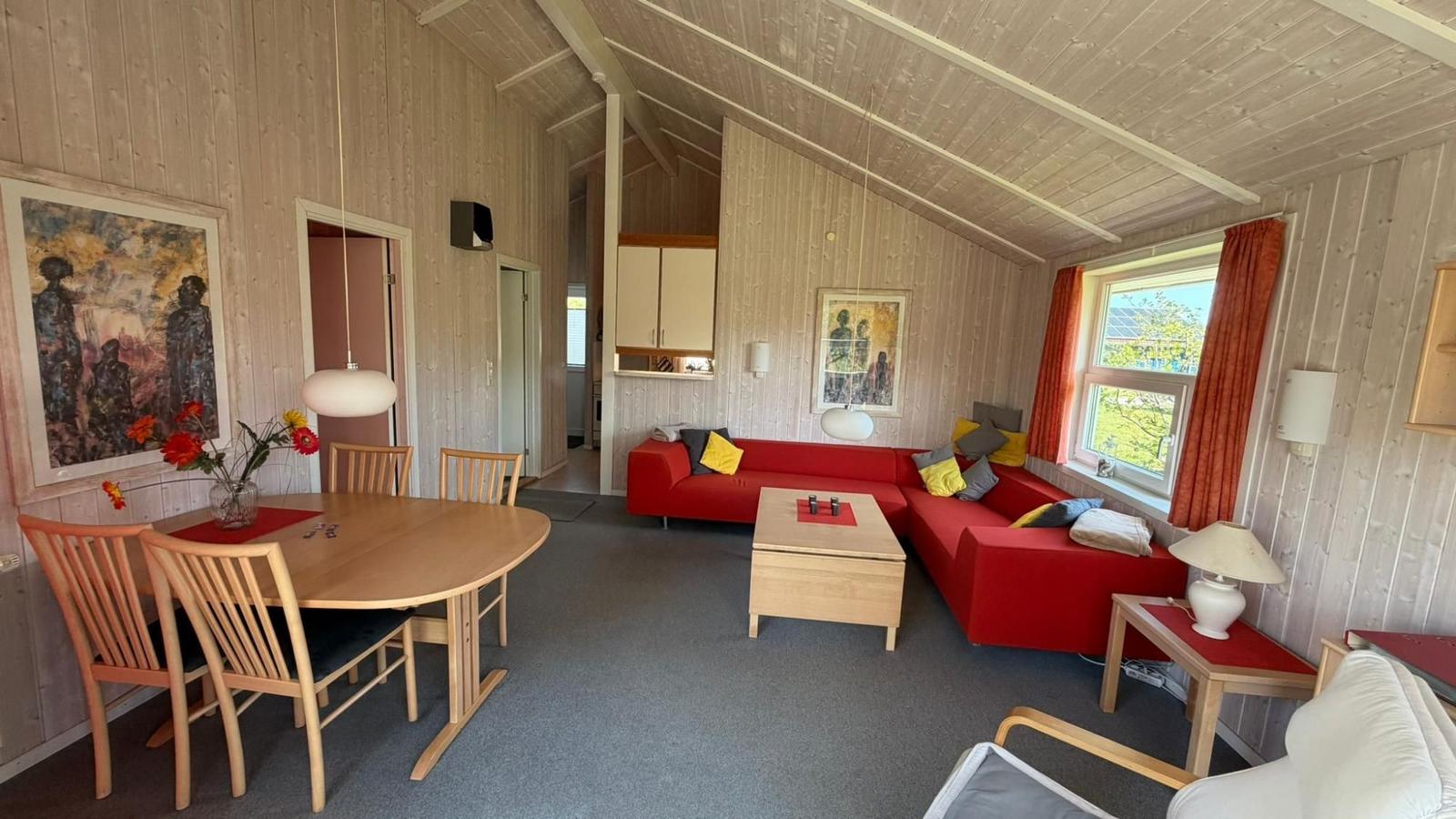 Wohn- und Essbereich mit rotem Sofa, Holztisch und Fenster mit roten Vorhängen.