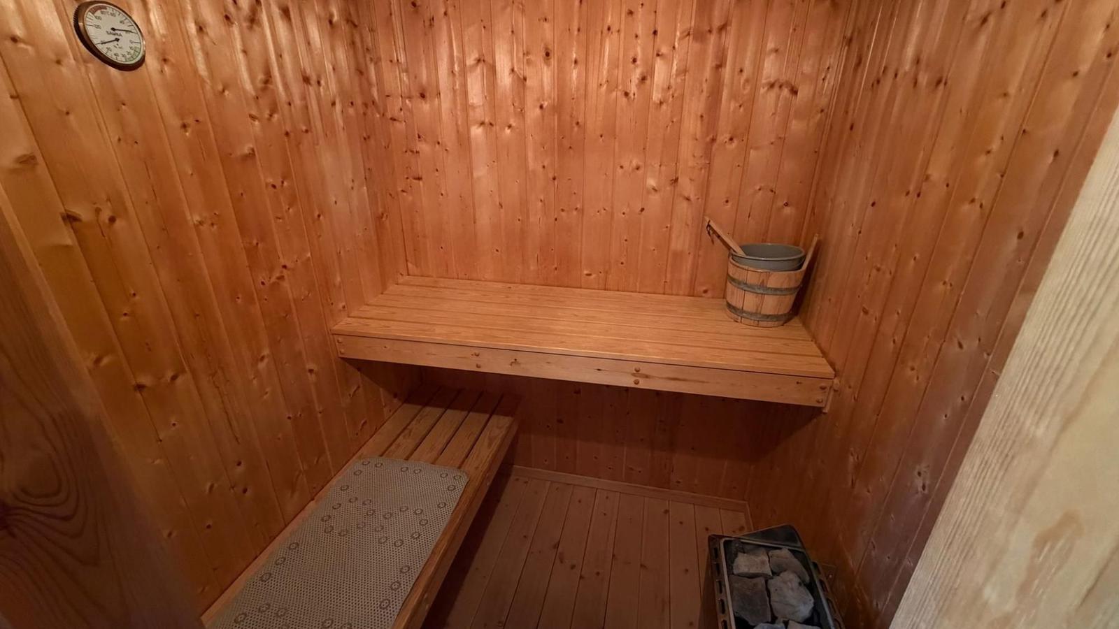 Sauna mit Holzwand, Bank, Eimer und Steinbecher.