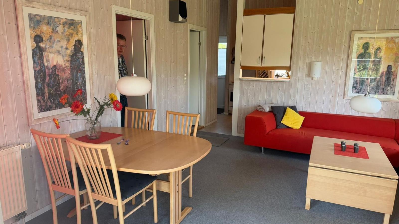 Essbereich mit Tisch und Stühlen. Wohnbereich mit rotem Sofa und Couchtisch.