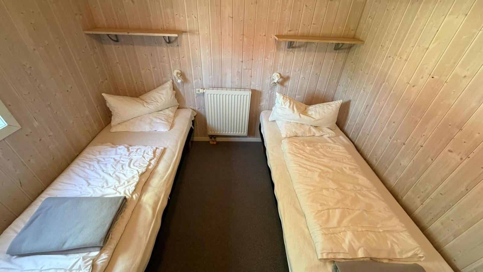 Zwei Einzelbetten mit Bettwäsche und Decken in einem Raum mit Holzwänden und Regalen.
