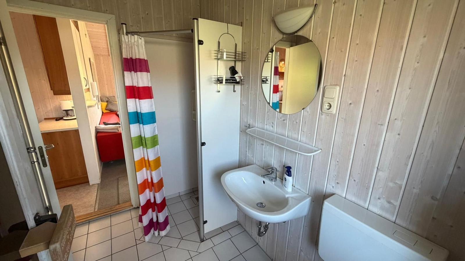 Badezimmer mit Waschbecken, Spiegel und Dusche mit buntem Vorhang.