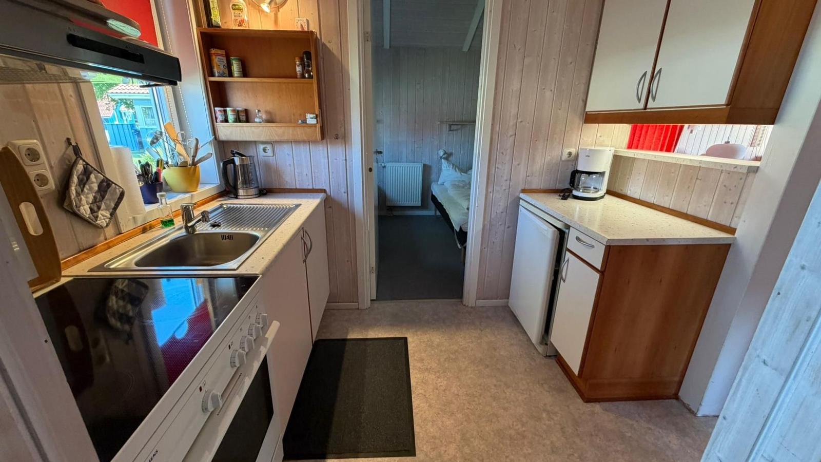 Küche mit Spüle, Herd und Kaffeemaschine. Im Hintergrund ist ein Schlafzimmer mit Bett sichtbar.