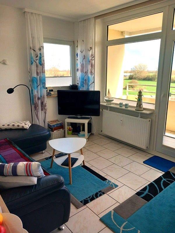 Wohnzimmer mit TV, Sitzgelegenheiten und Blick auf Balkon.