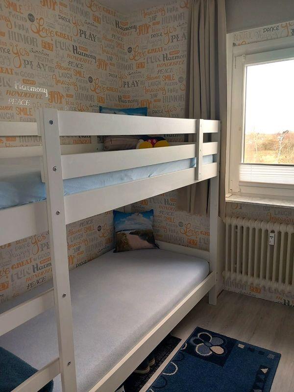 Zimmer mit Doppelstockbett und Fenster. Wandtapete mit Worten. Teppich auf dem Boden.