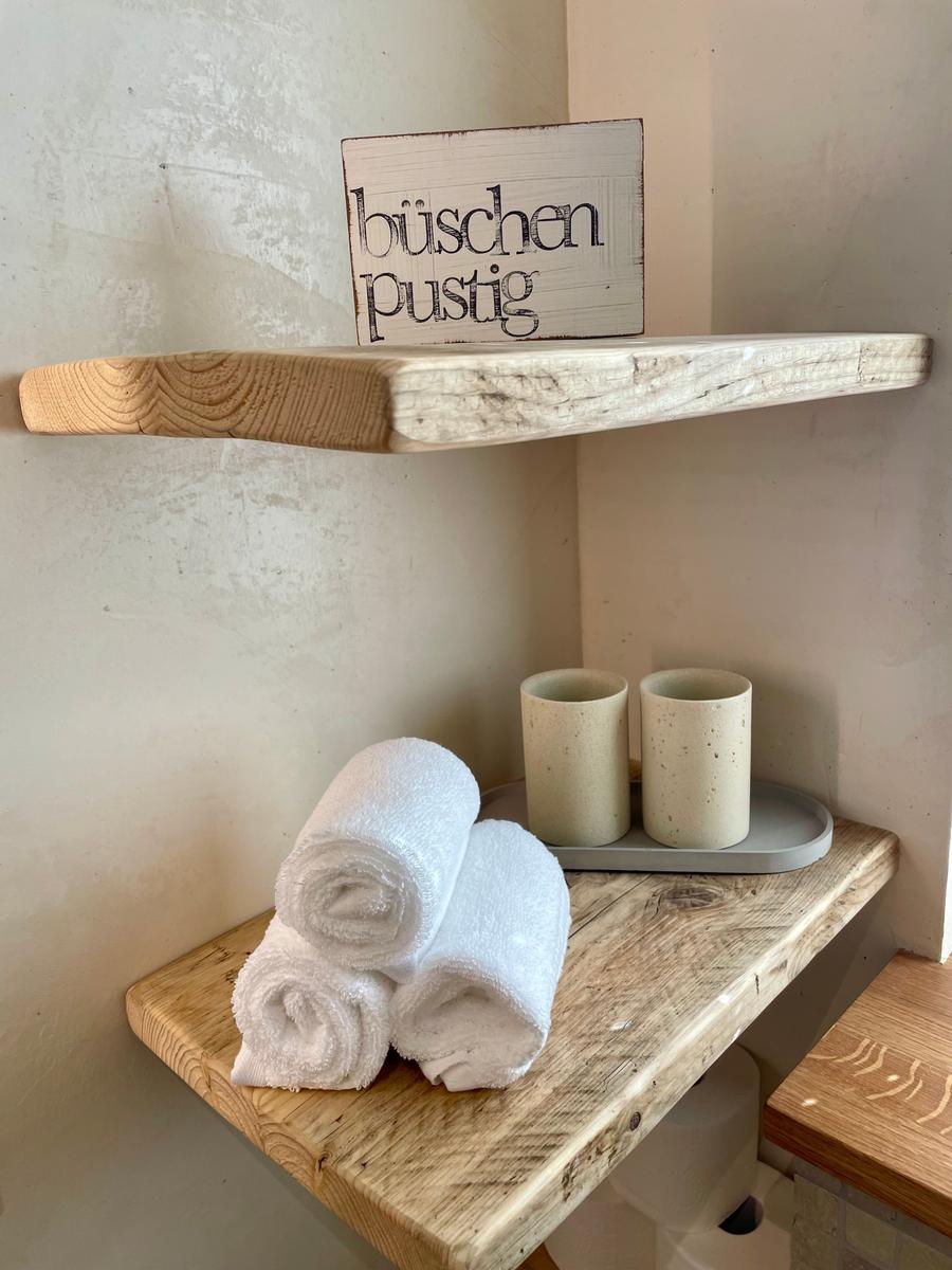 Holzregal mit Handtüchern und Keramikbechern. Schild mit Schriftzug büschen pustig.
