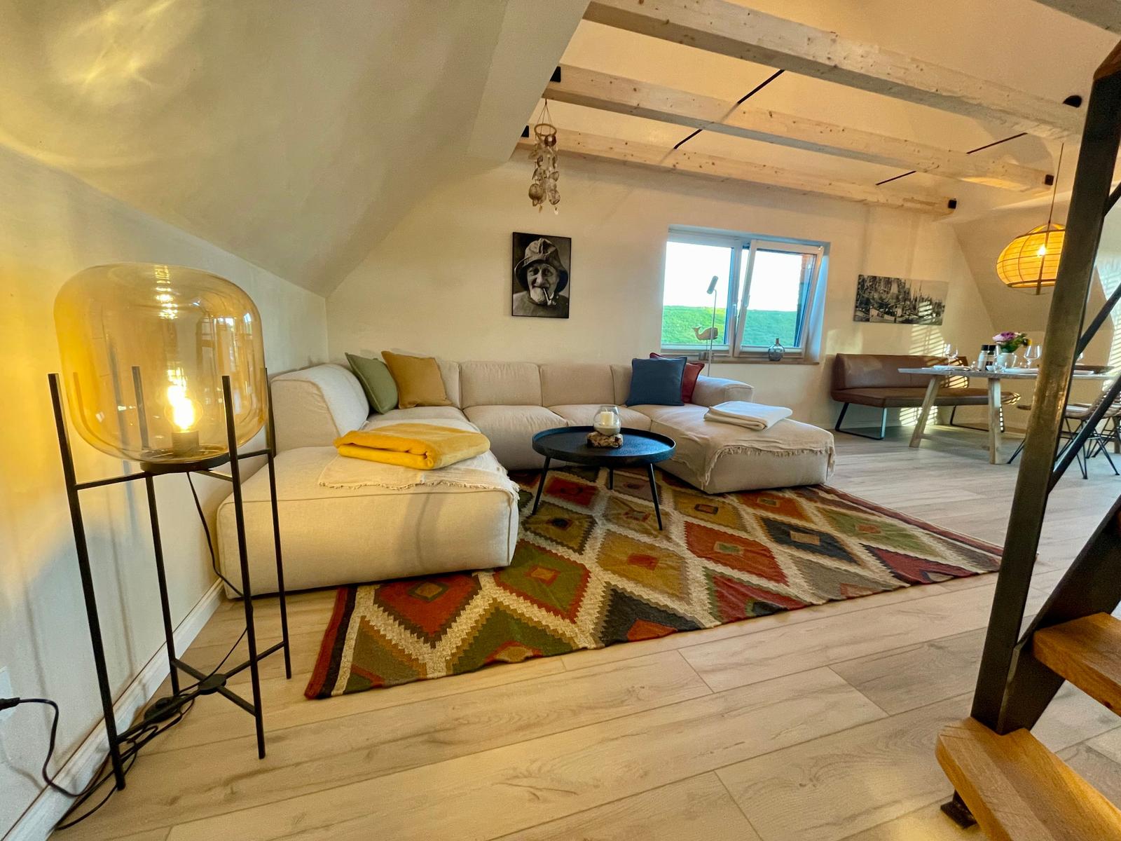 Wohnzimmer mit Sofa, Teppich und Lampe. Holzboden und Balken an der Decke.