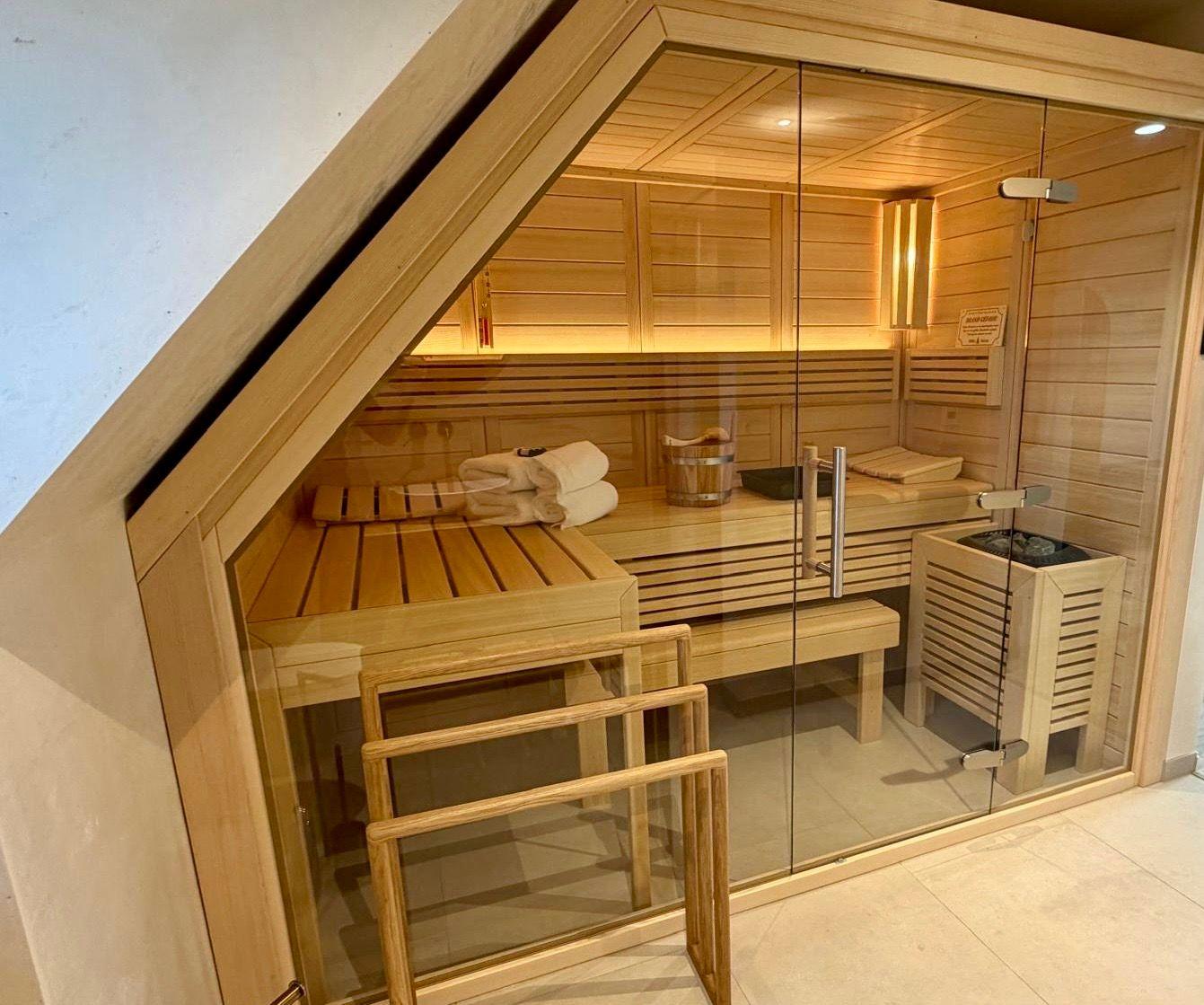 Sauna mit Holzbank, Handtuch und Heizung. Glasfront und Dachschräge sichtbar.