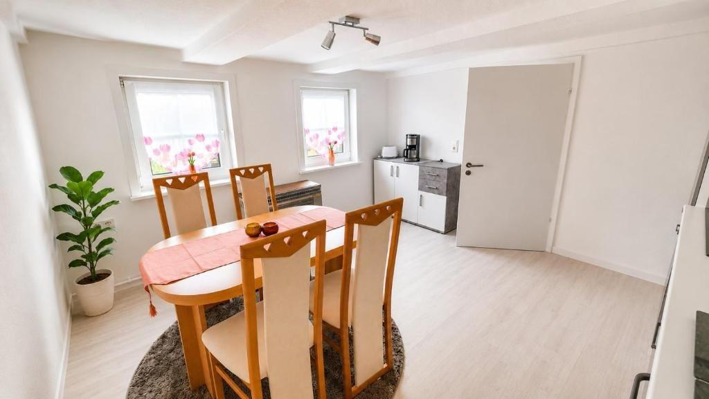 Essbereich mit Tisch, Stühlen und Pflanze. Küche und Tür im Hintergrund.