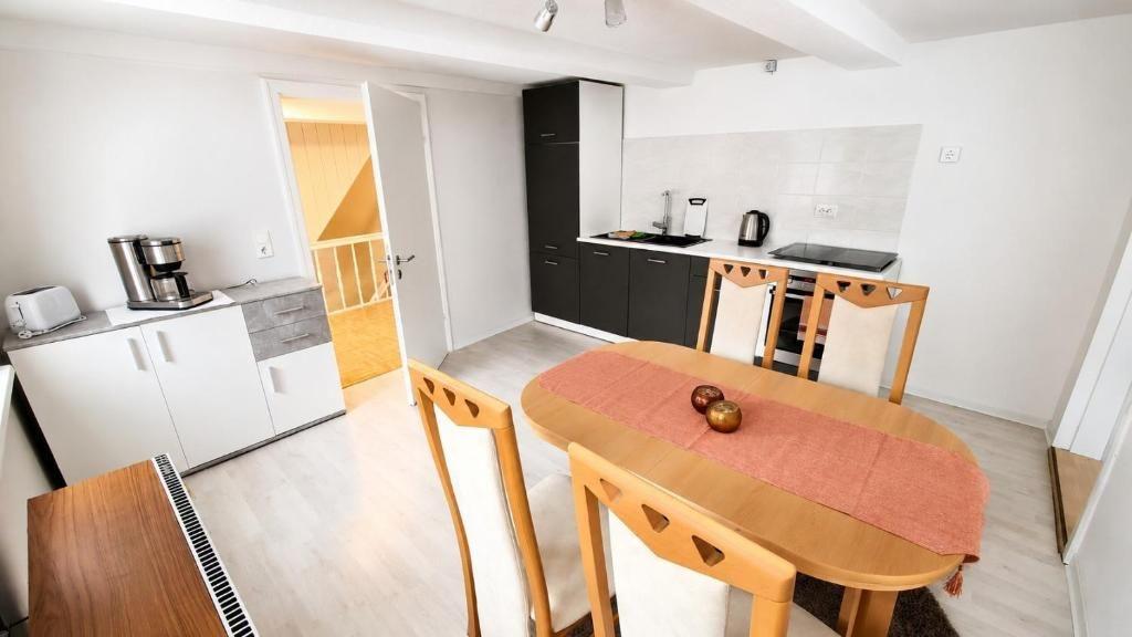 Essbereich mit Holztisch und Stühlen. Küche mit Arbeitsplatte und Geräten. Tür führt in einen Flur.