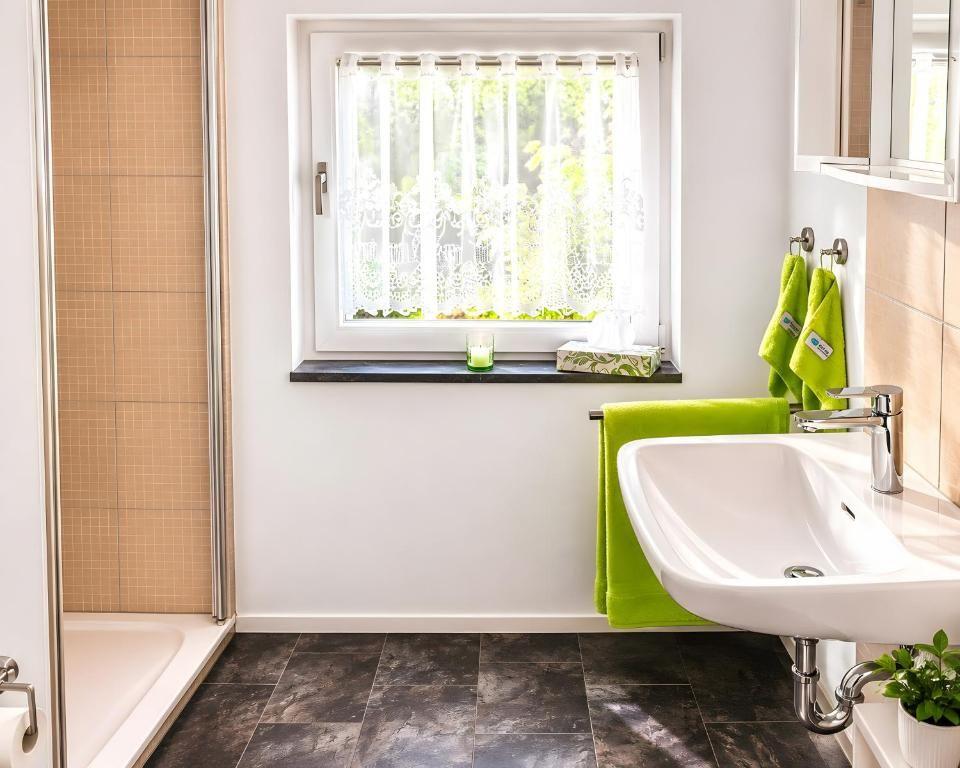 Badezimmer mit Dusche, Waschbecken und Fenster mit grünen Handtüchern.