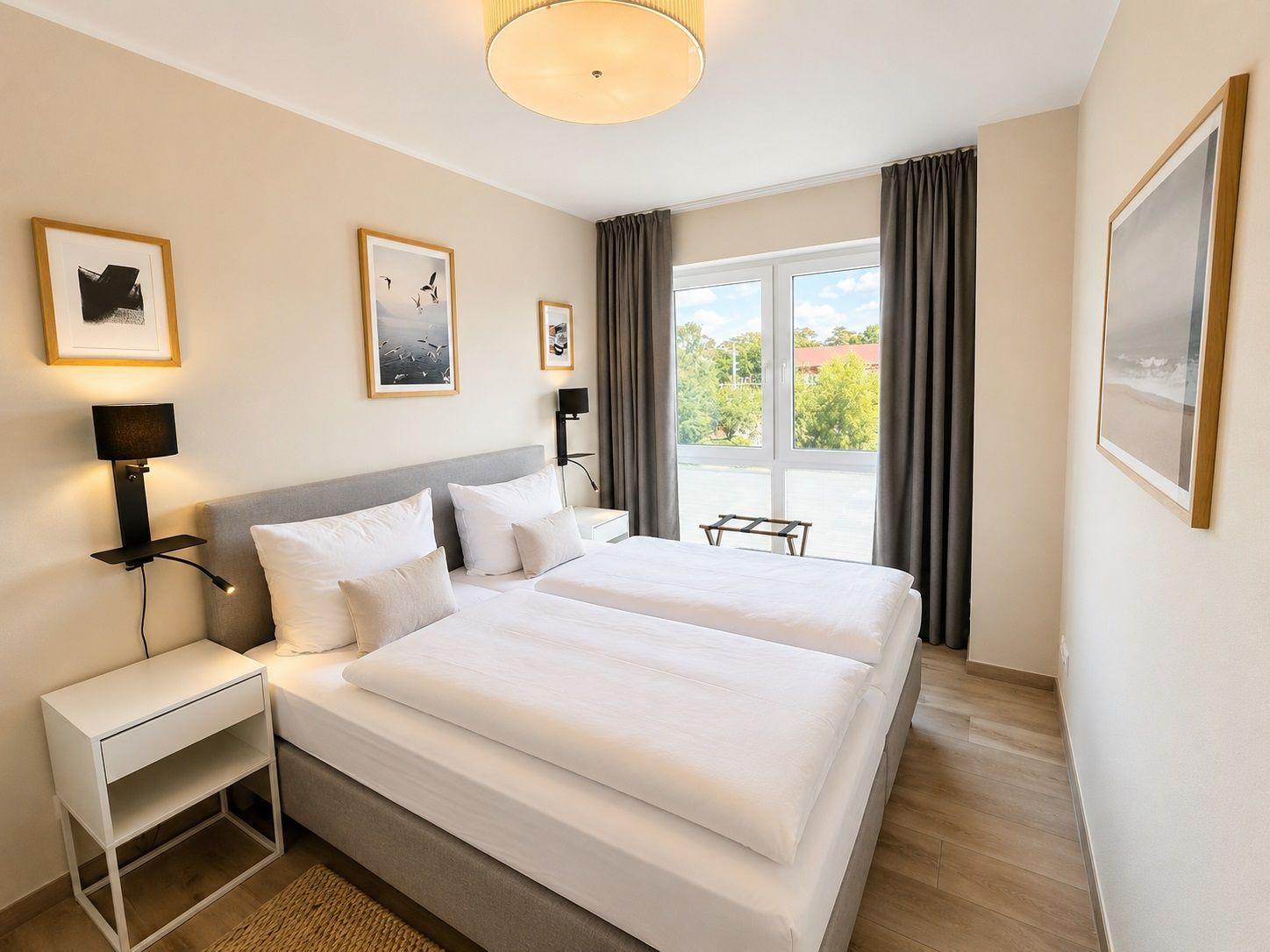 Schlafzimmer mit Doppelbett, Fenster und Wandbildern.