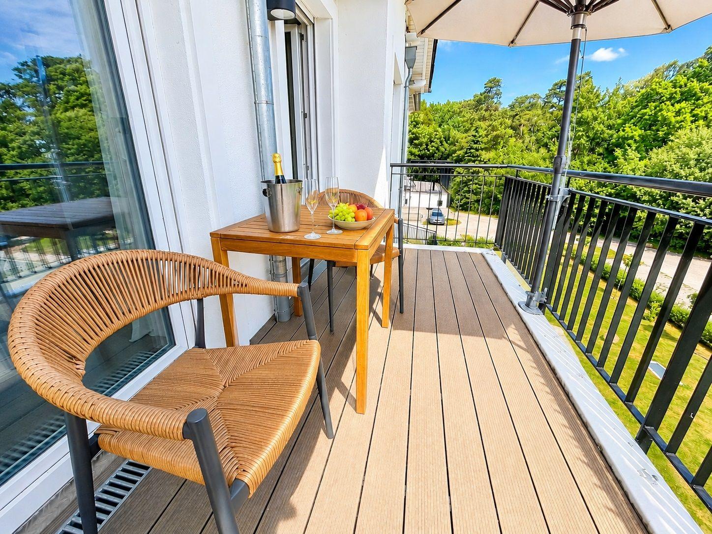 Terrasse mit Tisch, Stühlen und Sonnenschutz. Blick auf grüne Bäume und einen gepflegten Garten.