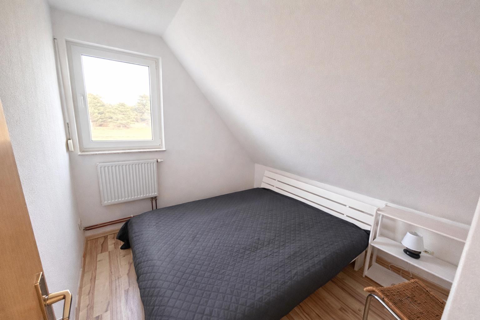 Schlafzimmer mit Dachschräge, Bett, Fenster und Nachttisch.