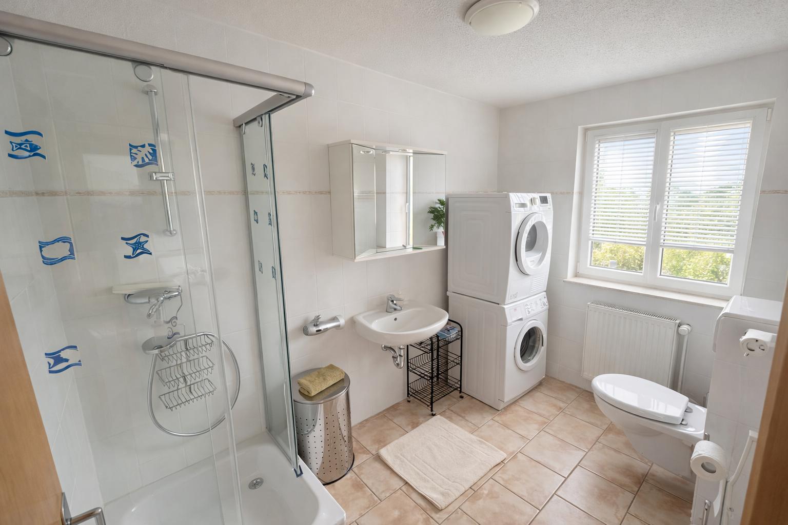 Badezimmer mit Dusche, Waschmaschine, Toilette und Fenster.