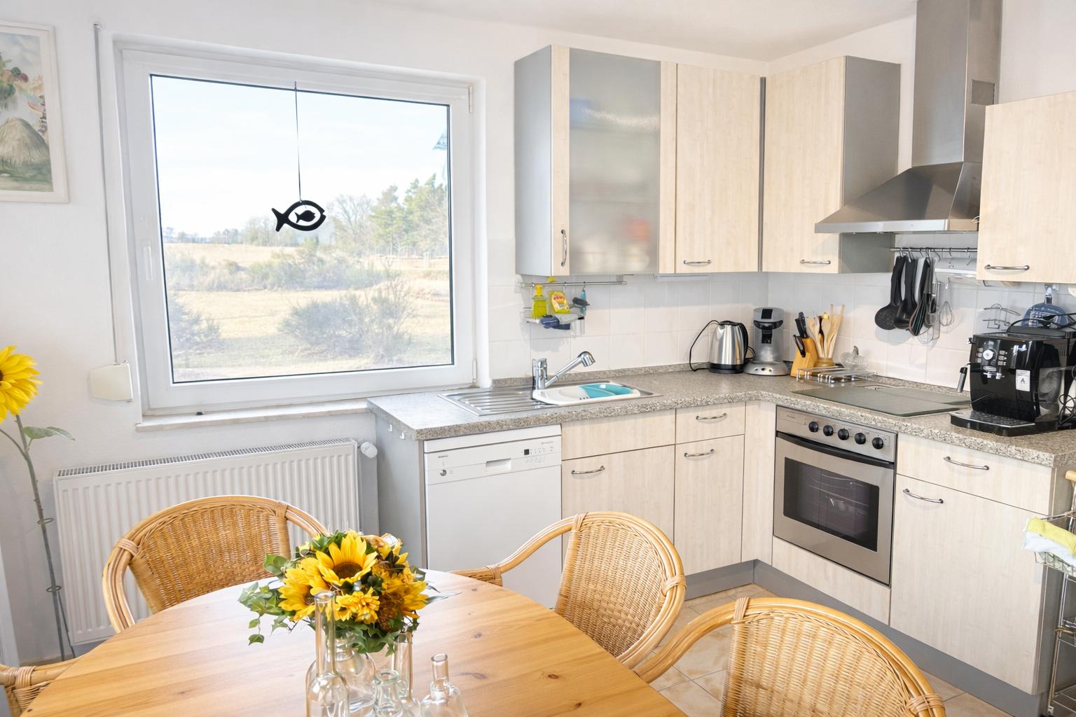 Küche mit Essbereich, Fensterblick auf Feld, Holztisch und Stühle, Edelstahlgeräte und Holzschränke.